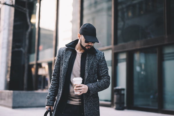 young-man-with-beard-wearing-trench-coat-standing-drinking-coffee